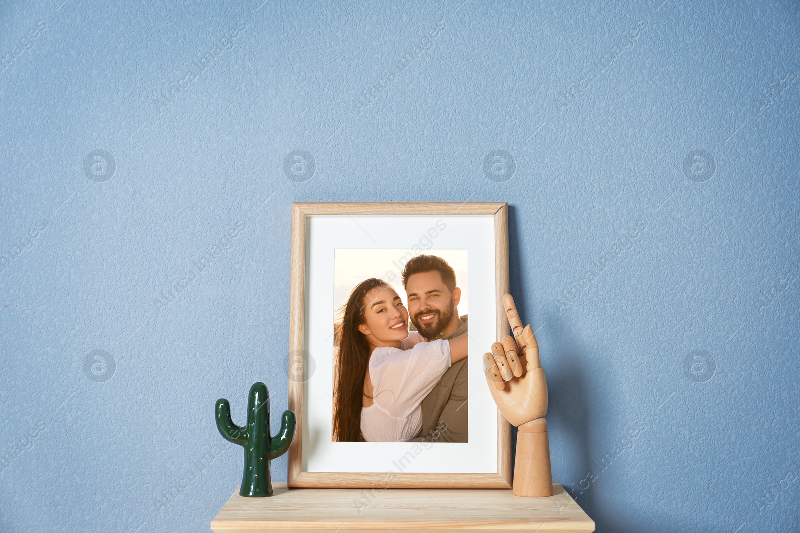 Image of Portrait of happy young couple in photo frame on table near light blue wall