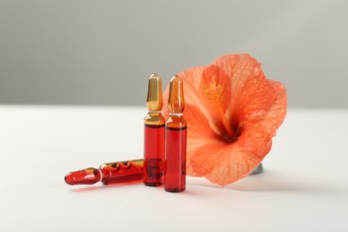 Skincare ampoules and hibiscus flower on white table