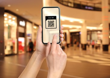 Woman holding smartphone with QR code on screen in shopping mall, closeup