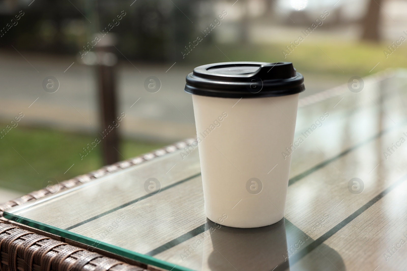 Photo of Paper takeaway cup on glass table outdoors. Coffee to go