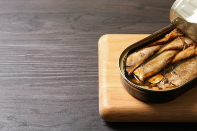 Board with tin can of sprats on wooden table, closeup. Space for text