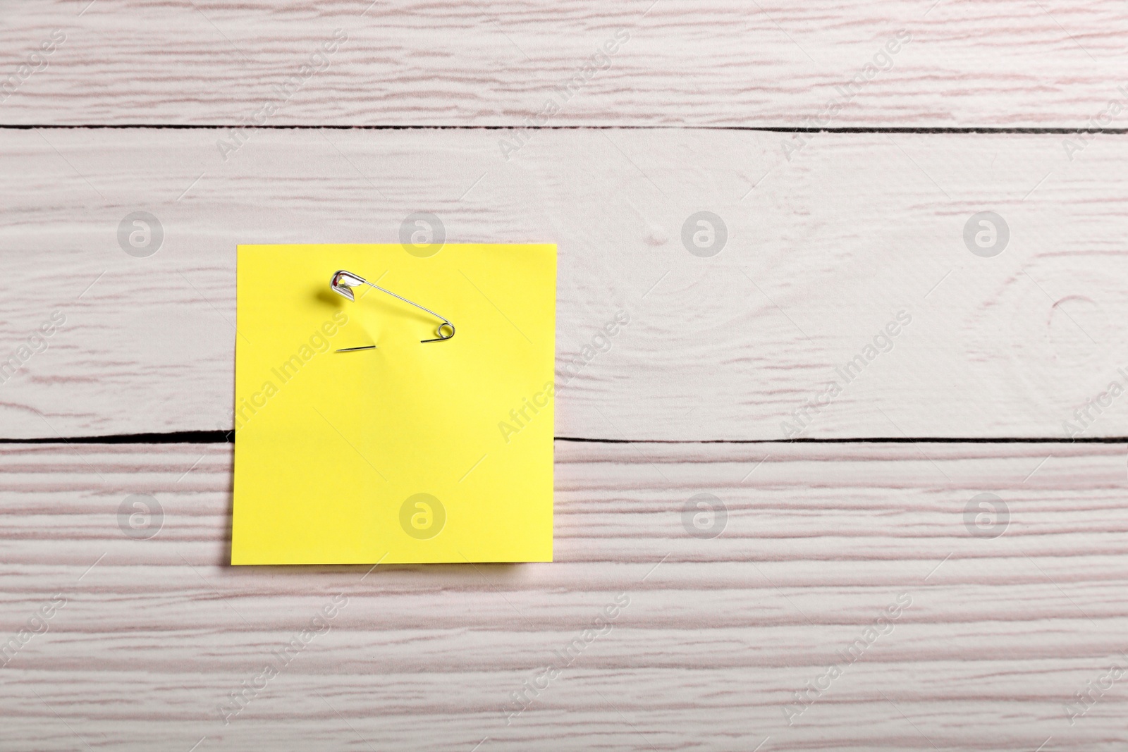 Photo of Yellow paper note attached with safety pin to white wooden background, top view. Space for text