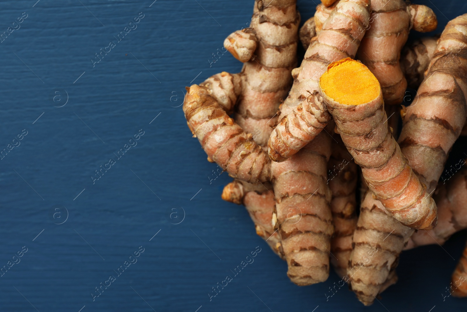 Photo of Pile of raw turmeric roots on blue wooden table, flat lay. Space for text