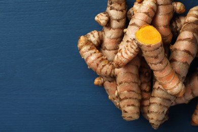 Pile of raw turmeric roots on blue wooden table, flat lay. Space for text