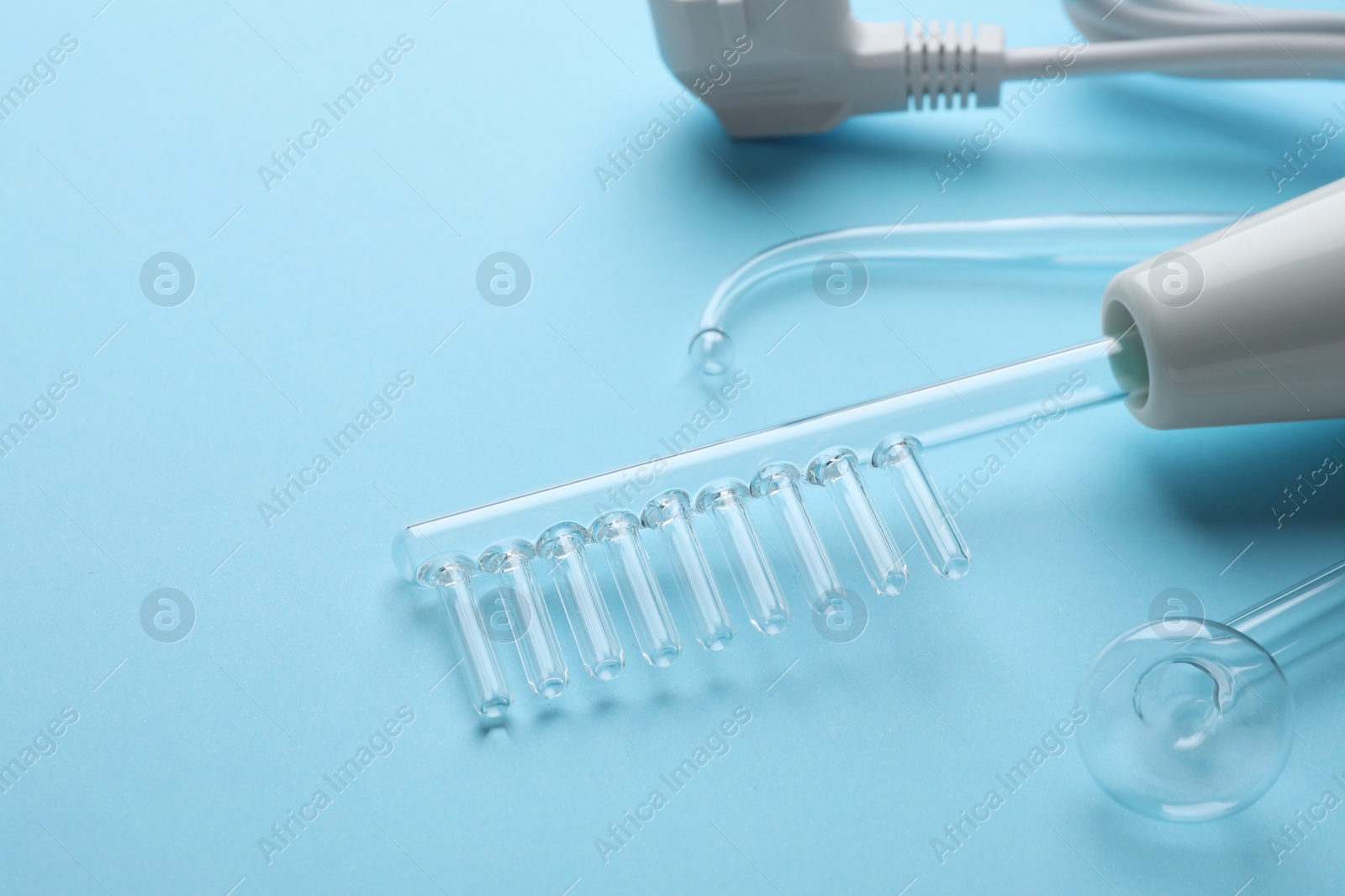 Photo of Modern darsonval with nozzles on light blue background, closeup. Space for text