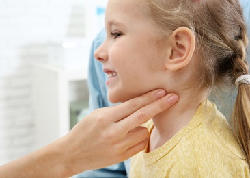 Young woman checking little girl's pulse with fingers indoors