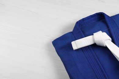 Photo of White karate belt and blue kimono on wooden background, top view. Space for text