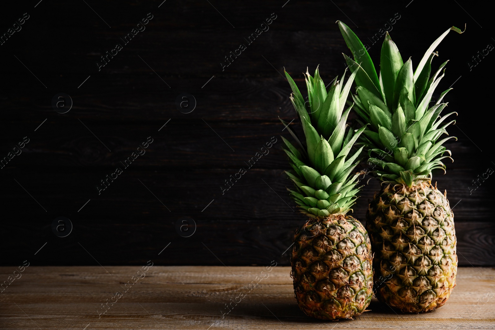 Photo of Fresh ripe juicy pineapples on wooden table. Space for text