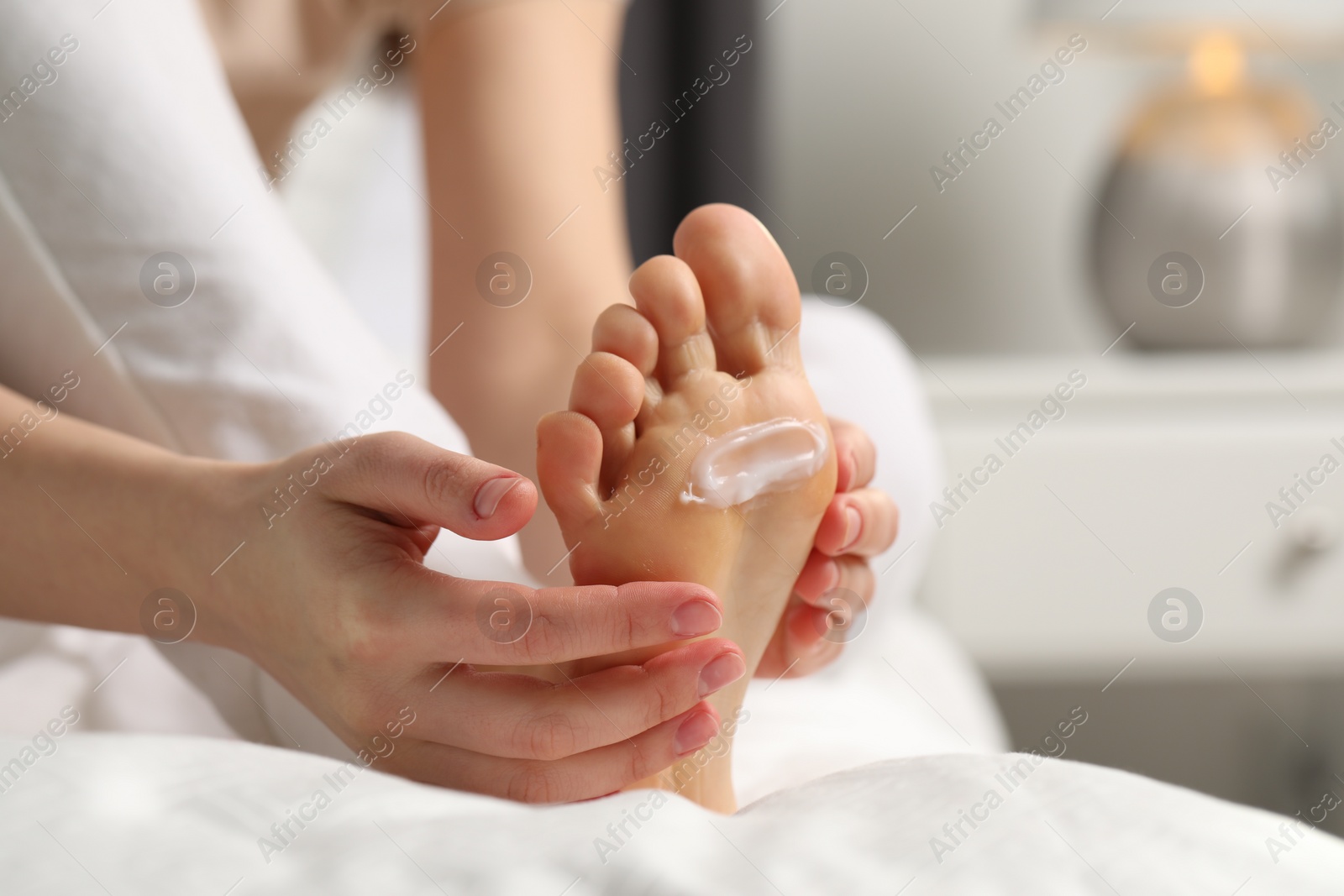 Photo of Young woman with dry skin applying cream onto her foot indoors, closeup