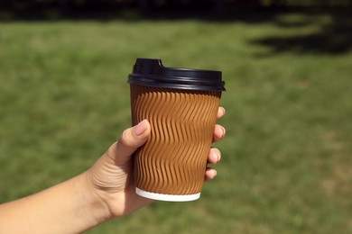 Woman holding takeaway cardboard coffee cup with plastic lid outdoors, closeup