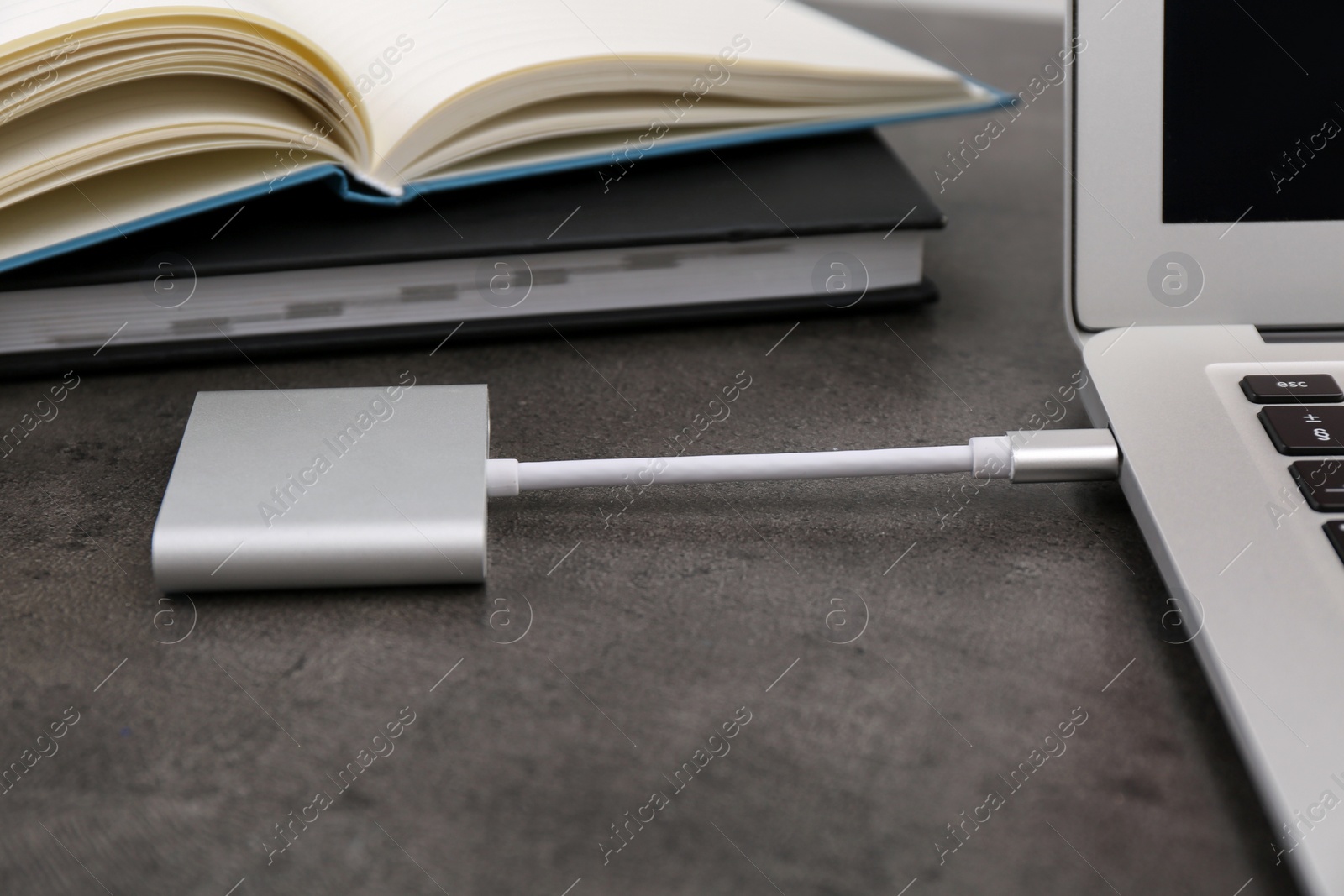 Photo of Charging modern laptop with power bank at grey table, closeup