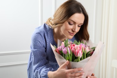 Photo of Happy young woman with bouquet of beautiful tulips indoors