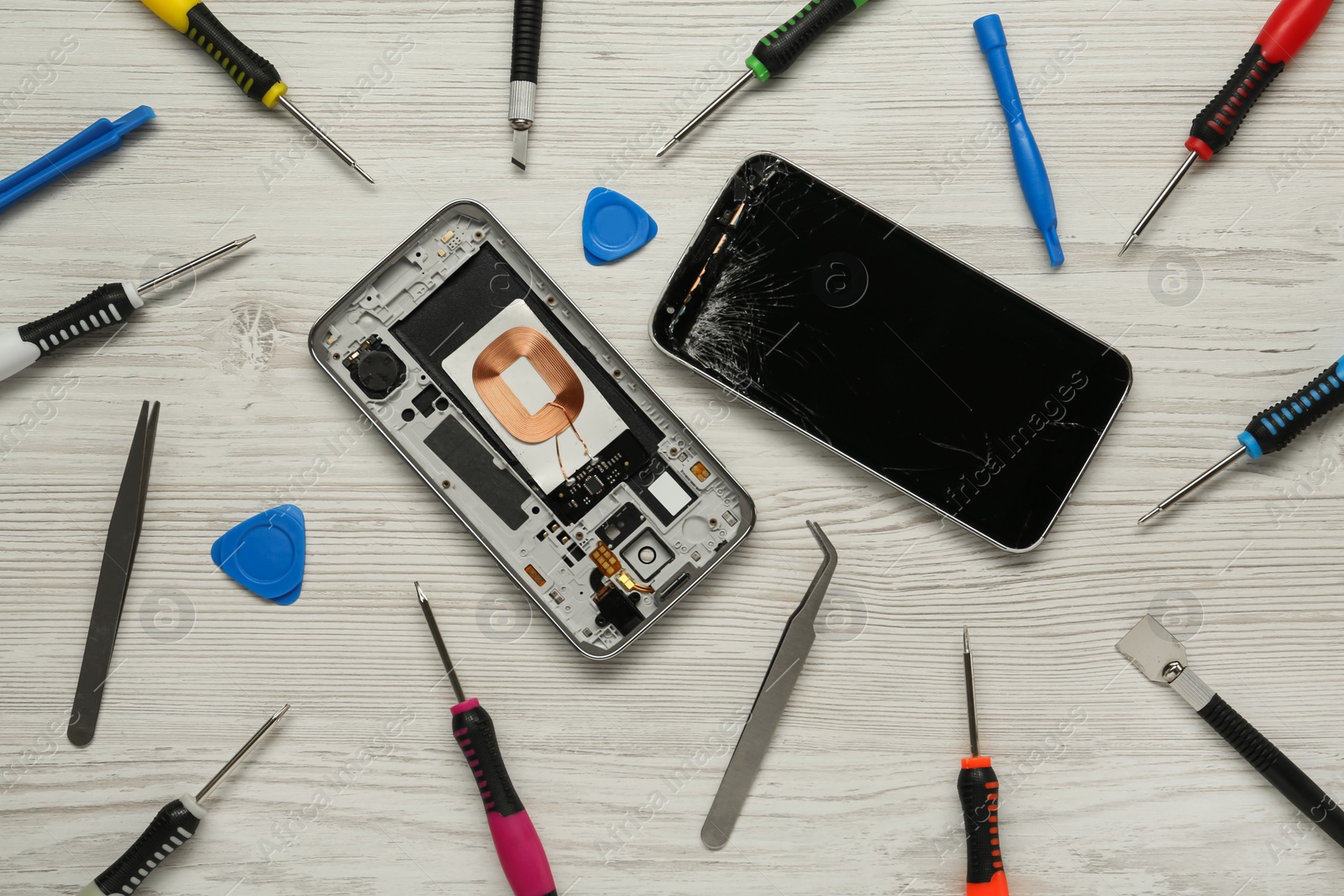 Photo of Damaged smartphone and repair tools on wooden background, flat lay