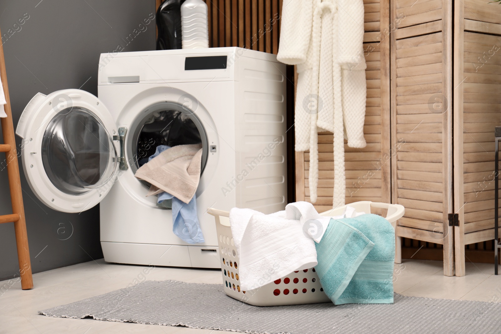 Photo of Basket with dirty towels on washing machine in modern laundry room