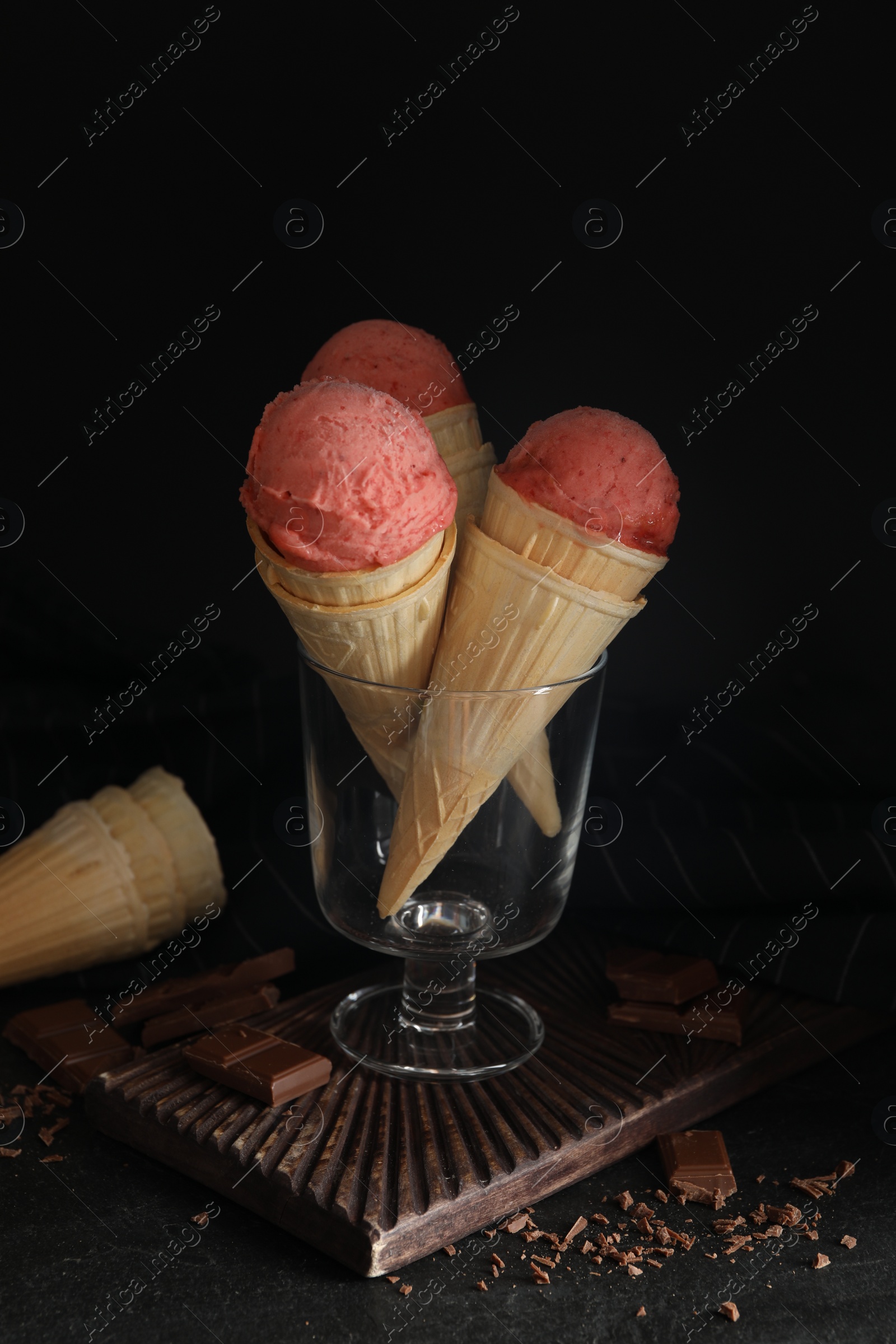 Photo of Delicious pink ice cream in wafer cones and chocolate on black table