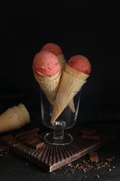 Delicious pink ice cream in wafer cones and chocolate on black table