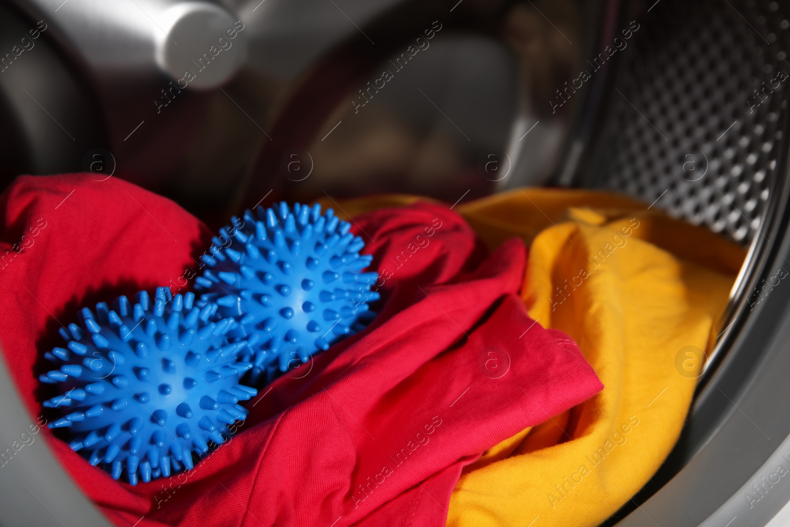 Photo of Blue dryer balls and clothes in washing machine drum, closeup