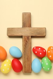 Wooden cross and painted Easter eggs on beige background, flat lay