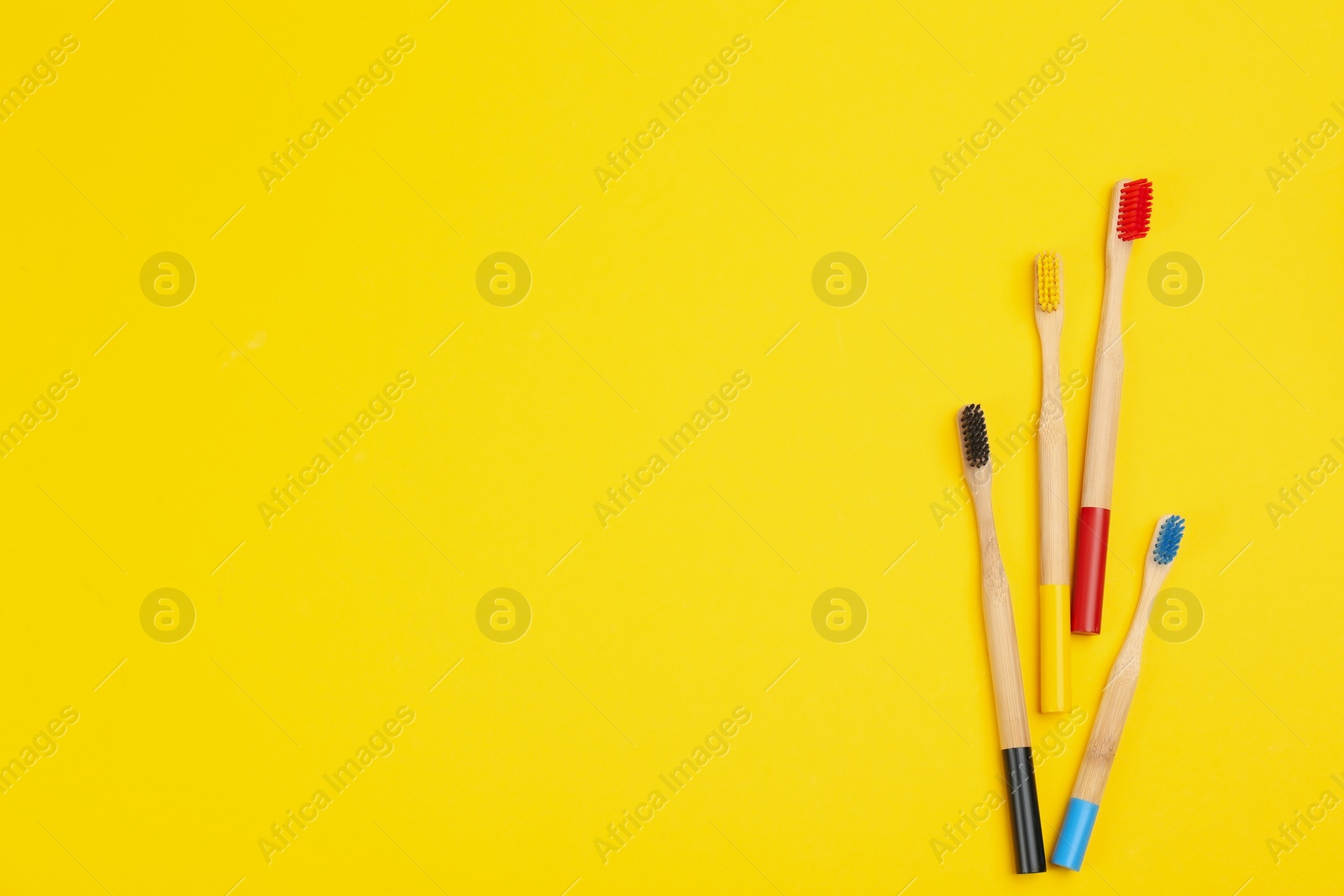 Photo of Toothbrushes made of bamboo on yellow background, flat lay. Space for text