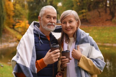 Photo of Affectionate senior couple with cups of coffee in autumn park