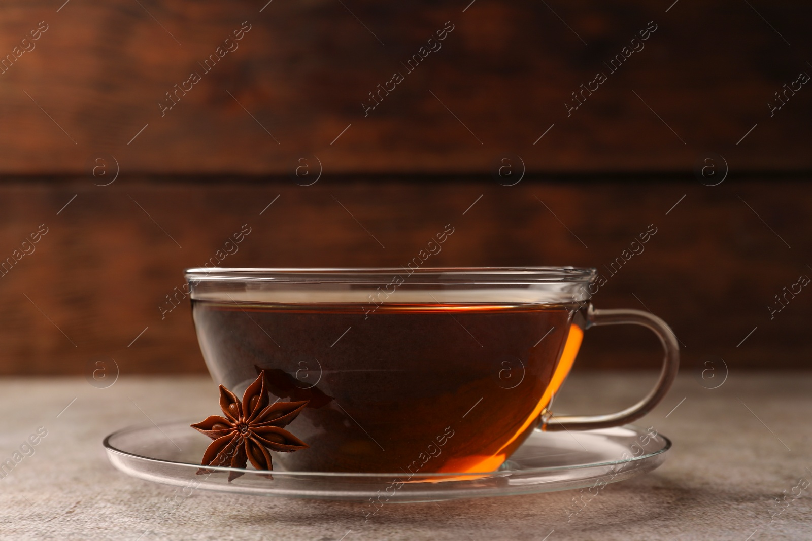 Photo of Glass cup of aromatic tea and anise star on light grey table, closeup