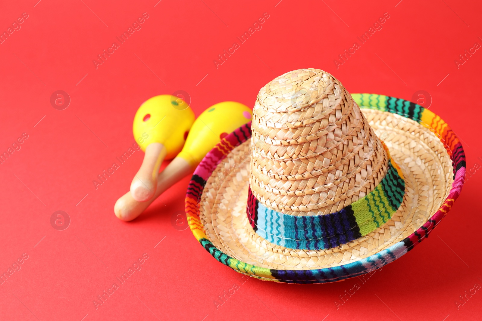 Photo of Mexican sombrero hat and maracas on red background. Space for text