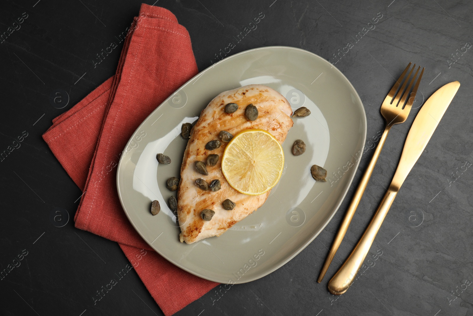 Photo of Delicious chicken fillet with capers and lemon served on black table, flat lay
