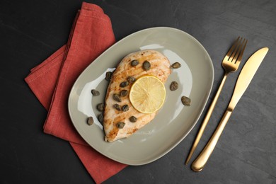 Photo of Delicious chicken fillet with capers and lemon served on black table, flat lay