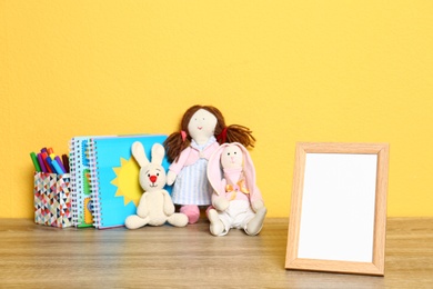 Photo of Soft toys and photo frame on table against yellow background, space for text. Child room interior