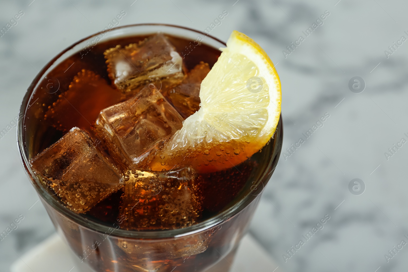 Photo of Glass of refreshing soda water with ice cubes and lemon slice on white table, closeup