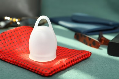Photo of White menstrual cup with red bag on green sofa, closeup. Space for text