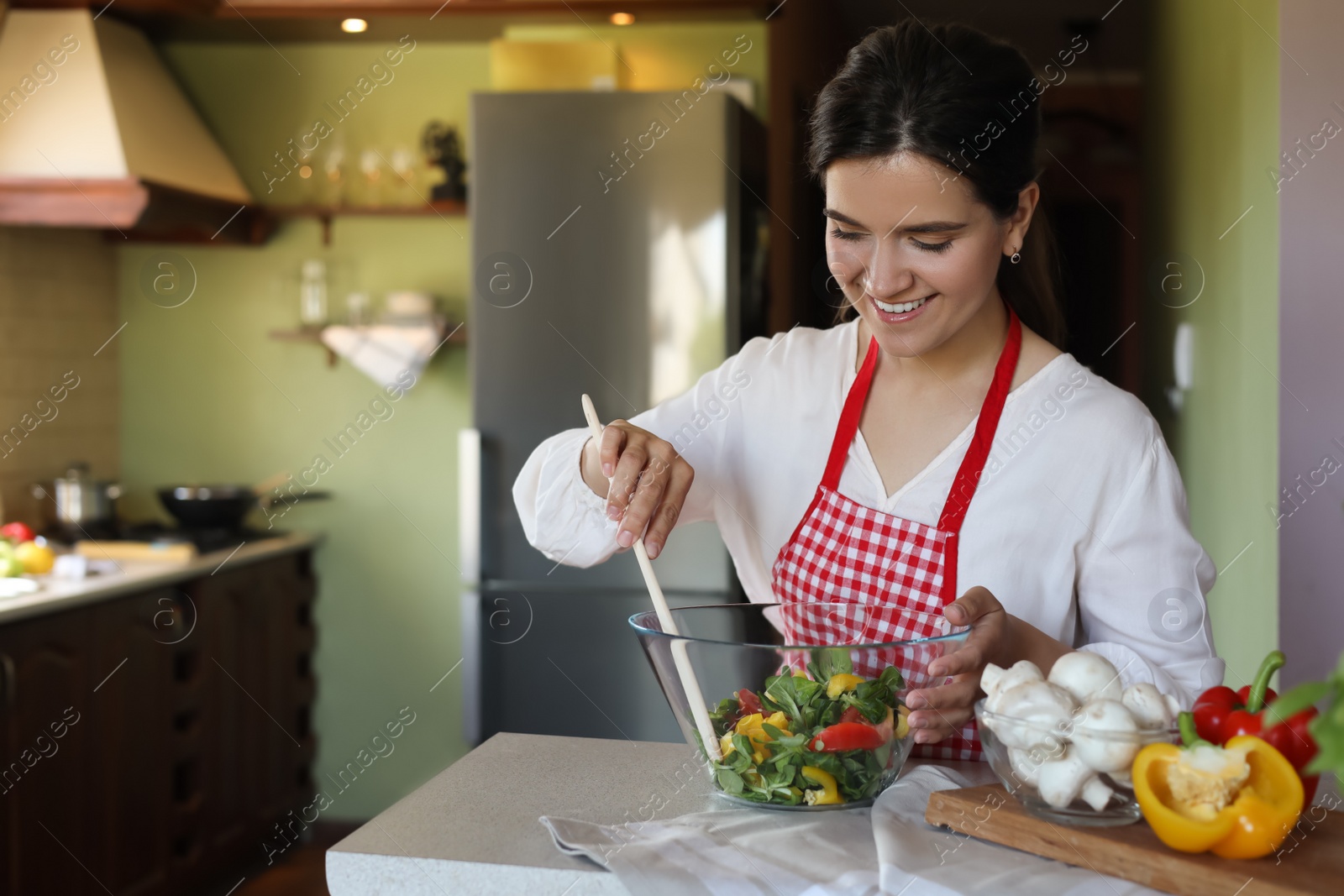 Photo of Young woman preparing salad at countertop in kitchen, space for text