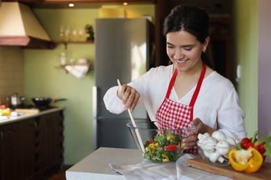 Photo of Young woman preparing salad at countertop in kitchen, space for text