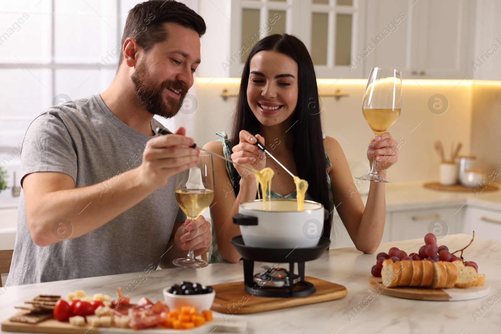 Photo of Affectionate couple enjoying cheese fondue during romantic date in kitchen