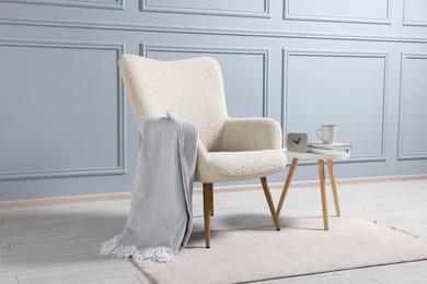 Photo of Comfortable armchair with blanket and side table indoors