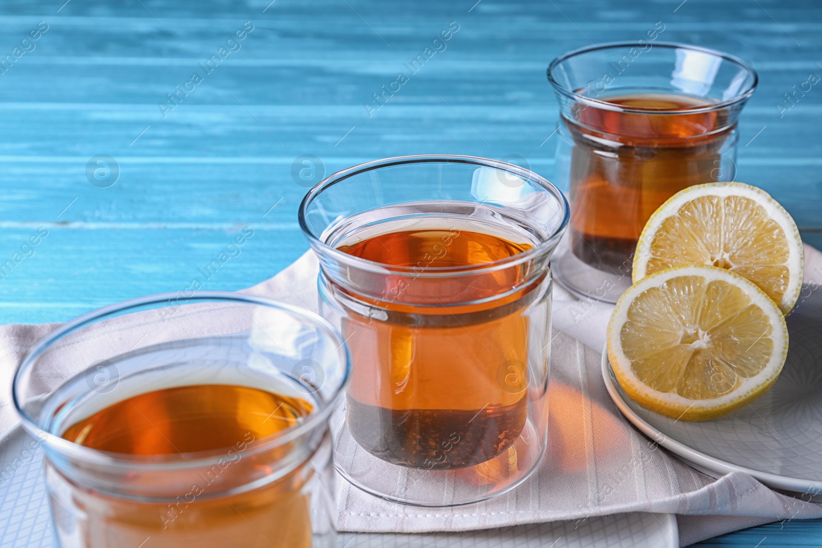 Photo of Plates with glasses of hot tea and lemon on blue wooden table