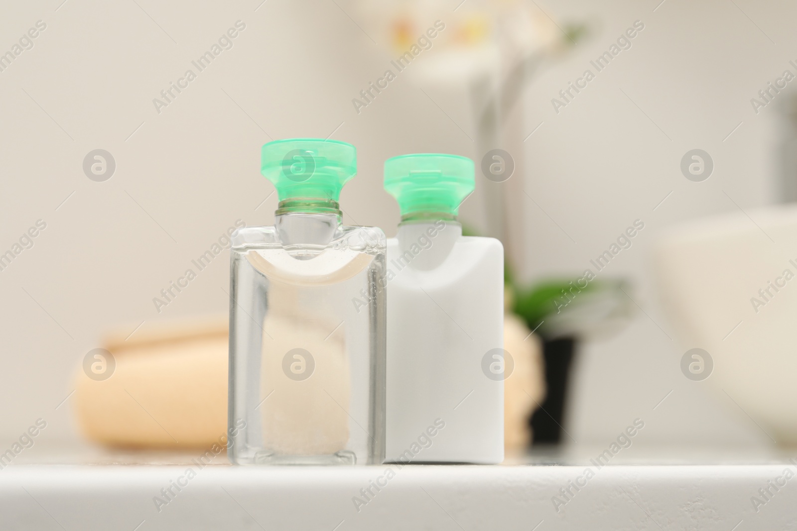 Photo of Mini bottles of cosmetic products on white table against blurred background