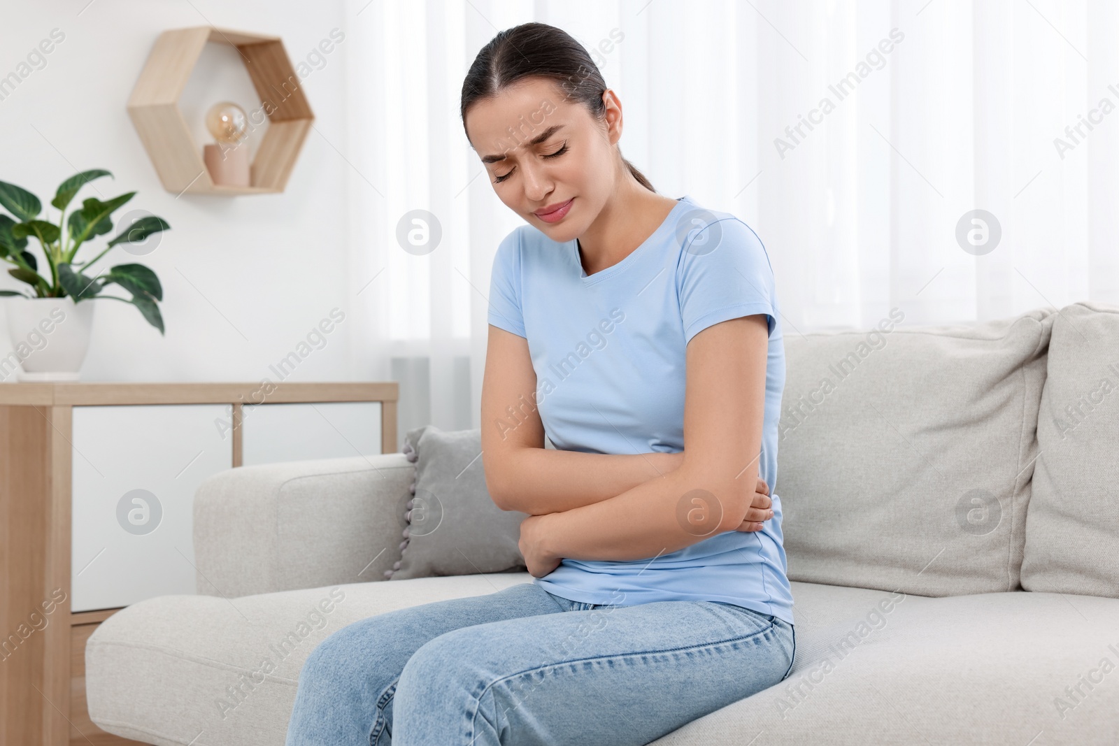 Photo of Woman suffering from abdominal pain on sofa at home. Unhealthy stomach