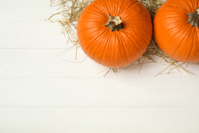 Photo of Ripe orange pumpkins and straw on white wooden table, flat lay. Space for text