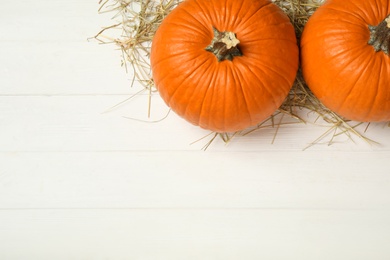 Ripe orange pumpkins and straw on white wooden table, flat lay. Space for text