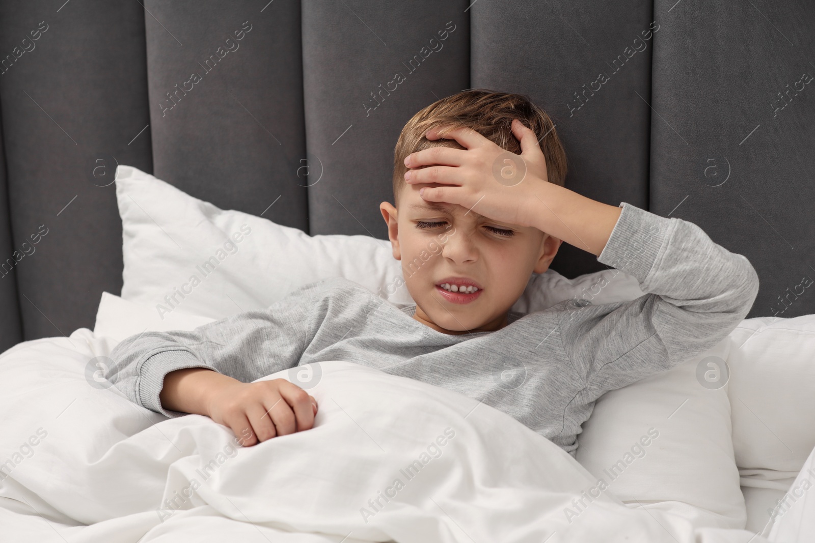 Photo of Little boy suffering from headache in bed at home