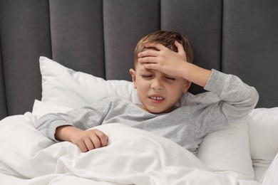 Photo of Little boy suffering from headache in bed at home