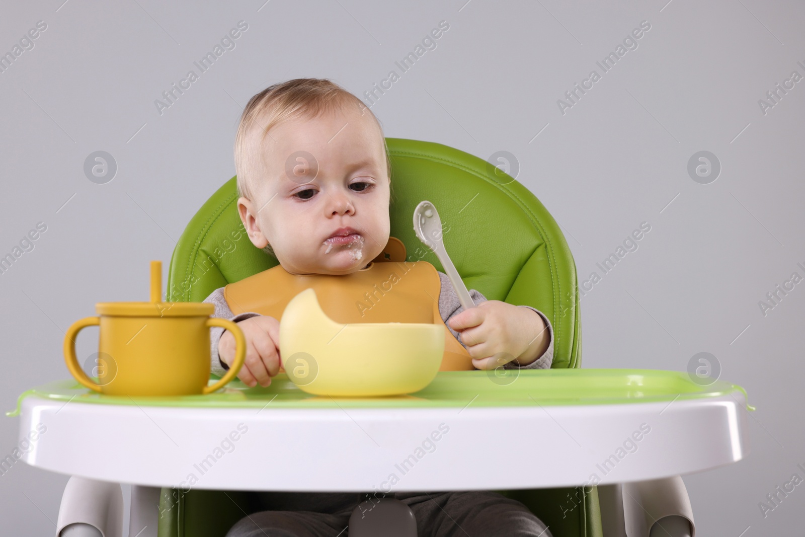 Photo of Cute little baby eating healthy food in high chair on gray background