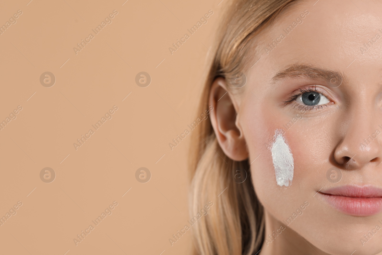 Photo of Beautiful young woman with sun protection cream on her face against beige background, closeup. Space for text