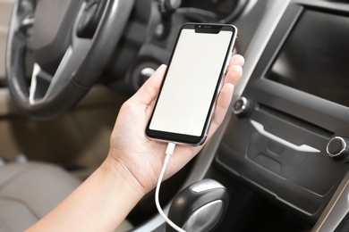 Woman connecting charging cable to smartphone in car, closeup