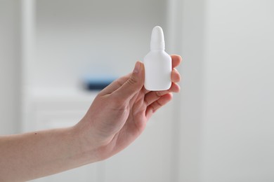 Photo of Woman holding nasal spray bottle indoors, closeup