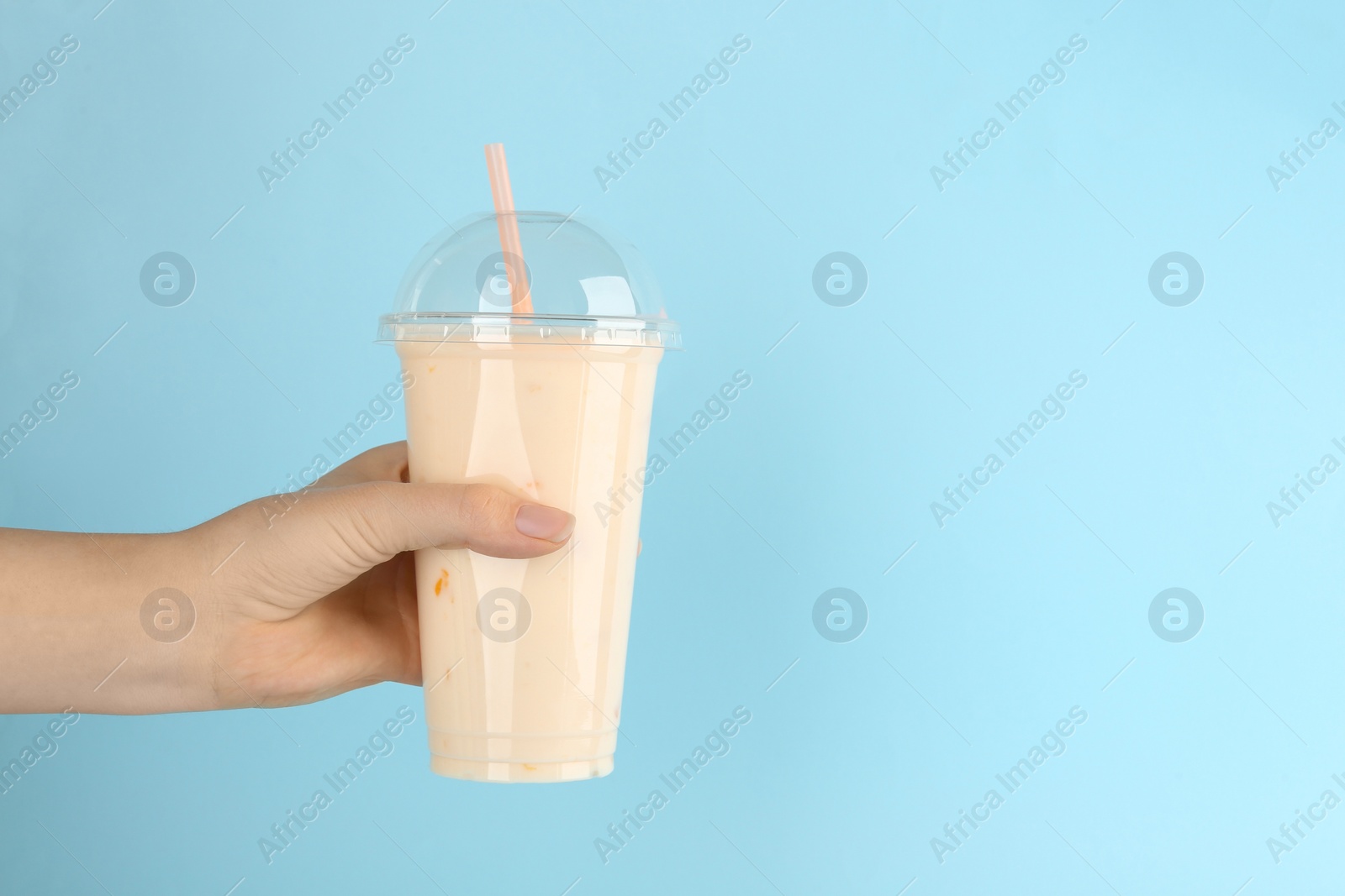 Photo of Woman with plastic cup of tasty smoothie on light blue background, closeup. Space for text