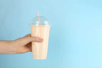 Photo of Woman with plastic cup of tasty smoothie on light blue background, closeup. Space for text