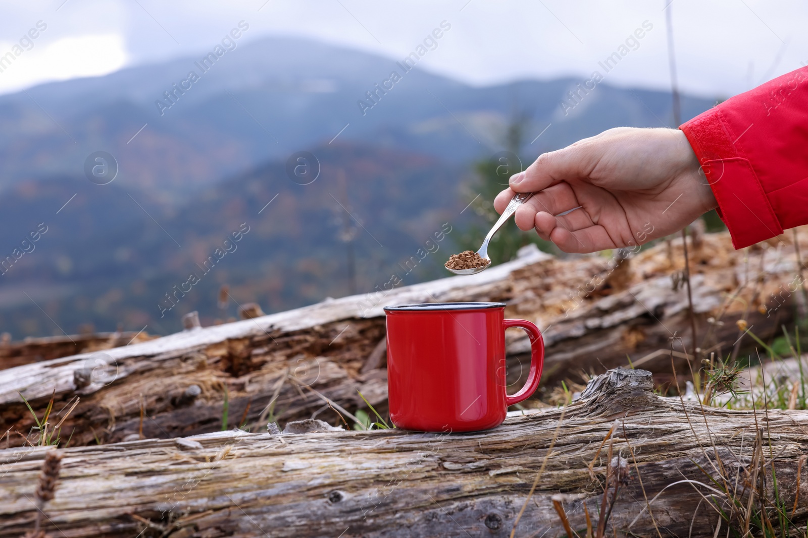 Photo of Woman pouring instant coffee into mug in mountains, closeup. Space for text