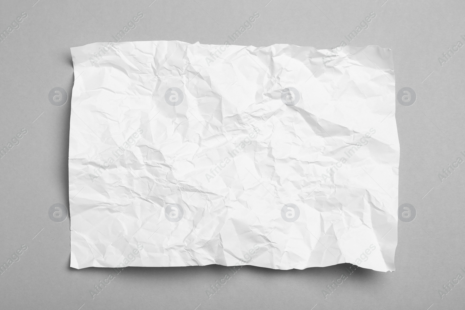 Photo of Sheet of white crumpled paper on grey background, top view